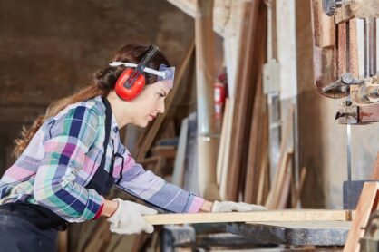 A female carpentry apprentice works with timber and a saw