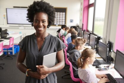 A black female teacher stands at the front of her classroom