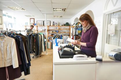 A charity volunteer stands behind the counter in a charity shop