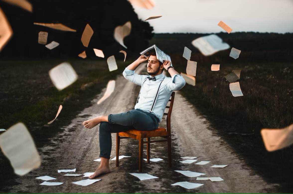 A barefooted man sits on a chair with papers around him