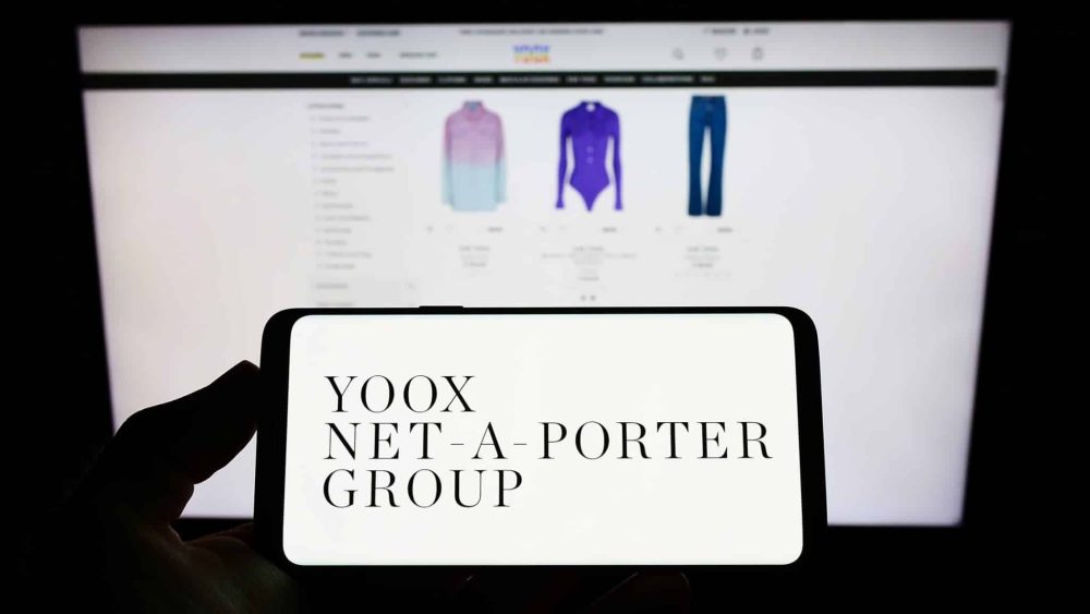 Person holding smartphone with logo of company Yoox Net-a-Porter Group