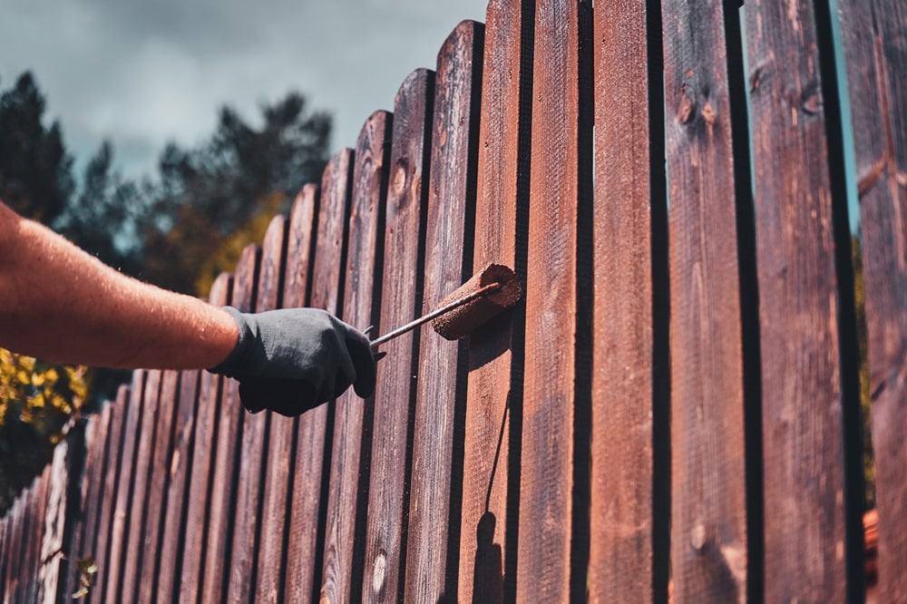 A man paints a fence using a roller