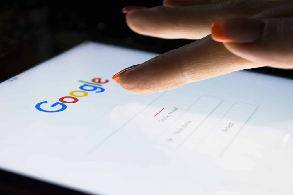A woman`s hand touching screen displaying google search engine on iPad Pro