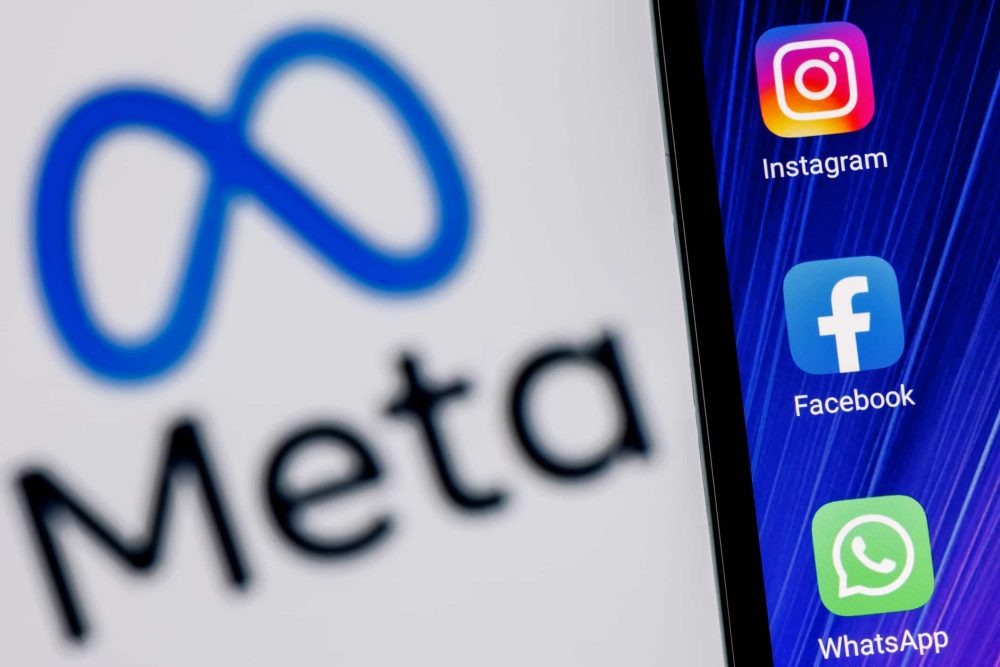 Meta logo and sign displayed on phone and Facebook, Instagram, and WhatsApp in the background
