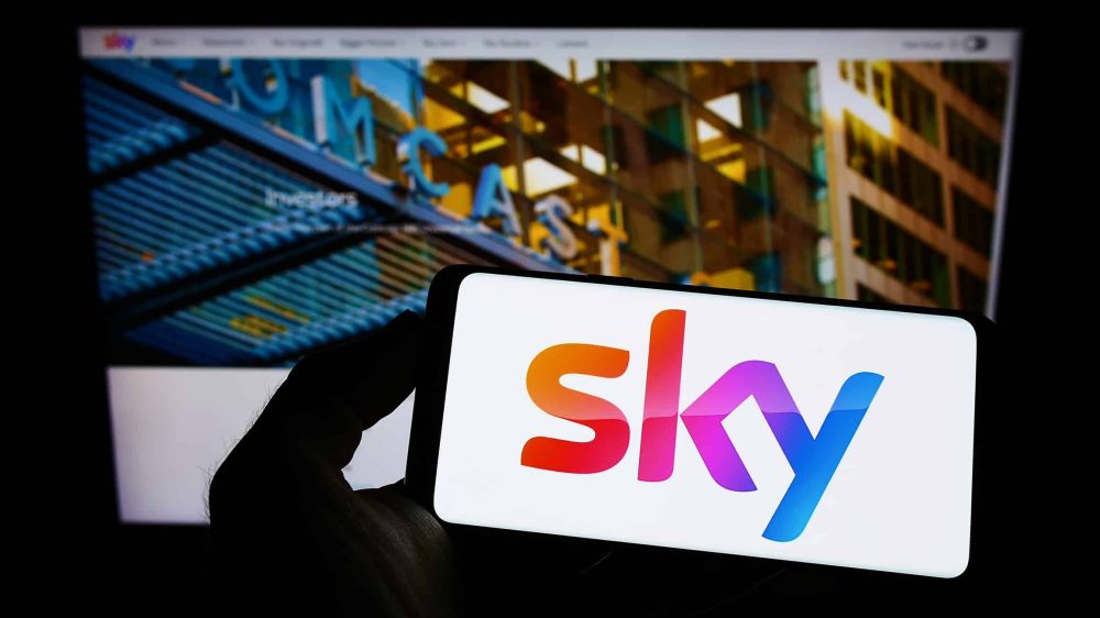 Sky group logo on phone with the background of Comcast website