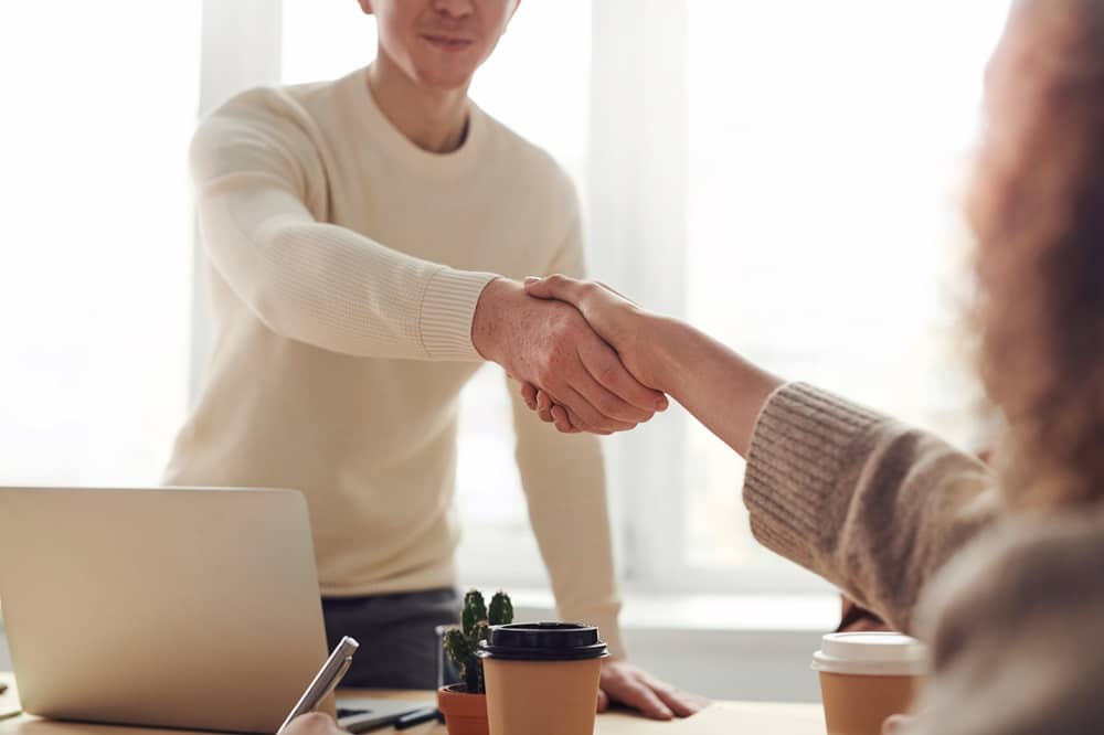Two people shaking hands with a laptop in view