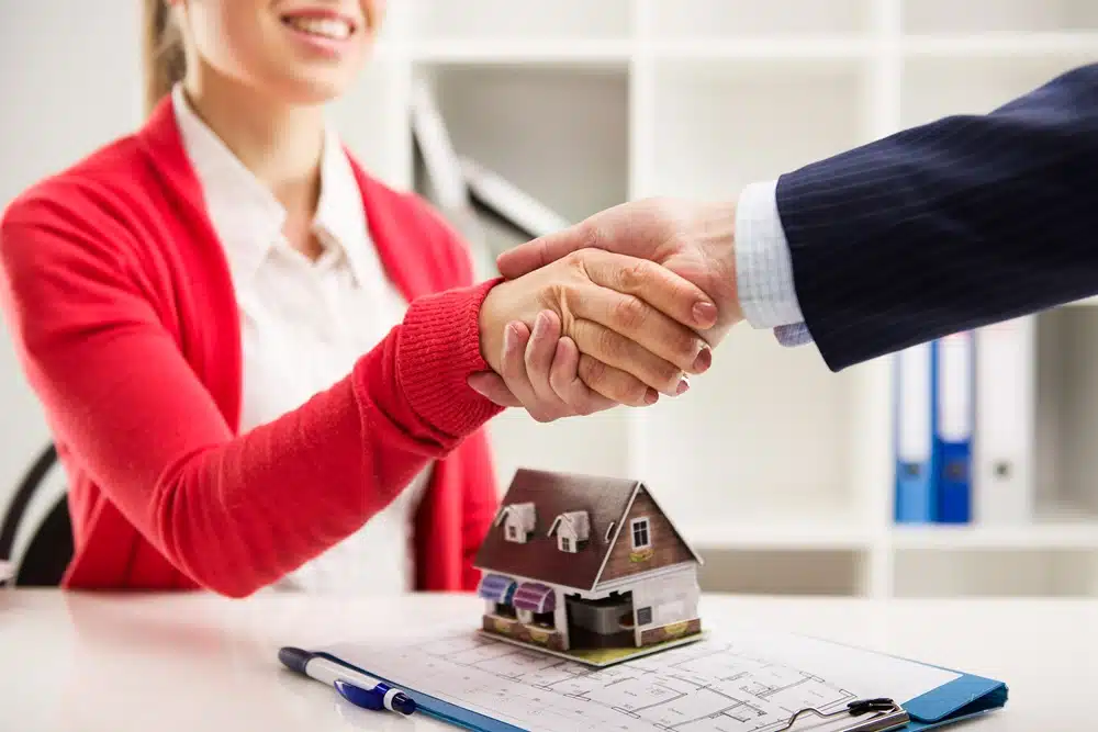 Woman shaking hands with a man over a little model of a house and a contract