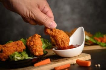 Hand holding fried chicken dipped in tomato sauce