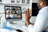 Video call, online conference. Over shoulder view of man at computer screen with multinational group of successful business people, virtual business meeting, work from home concept
