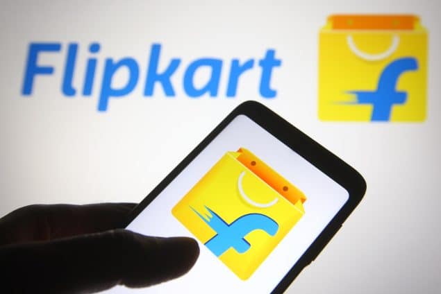 Flipkart logo is seen on a mobile phone in a hand and a computer screen