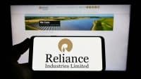 Hands holding phone with logo of Reliance Industries Limited on screen in front of the business webpage.