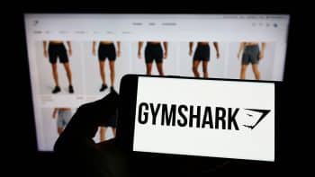 Person holding a cellphone displaying Gymshark Limited's logo with its business webpage in the background.
