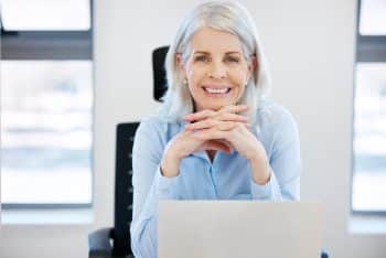 A grey-haired woman sits at her laptop